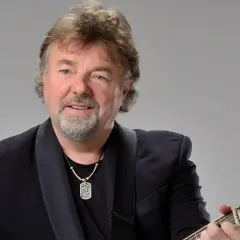 Mariusz Kalaga w czarnym garniturze gra na gitarze.