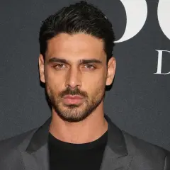 Michele Morrone w szarej marynarce i czarnej koszulce na tle napisu "DNI".