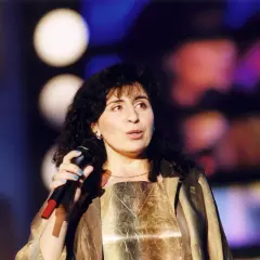 Eleni śpiewa na scenie, trzymając mikrofon.