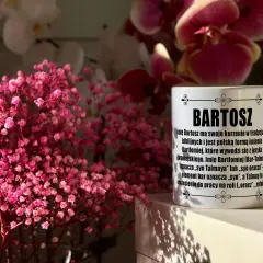Biały kubek z napisem "Bartosz" na tle różowych kwiatów i storczyków.