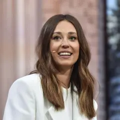 Izabella Krzan w białej marynarce, uśmiechnięta, z mikroportem przy uchu.