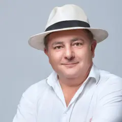 Portret Roberta Makłowicza w białej koszuli i słomkowym kapeluszu.