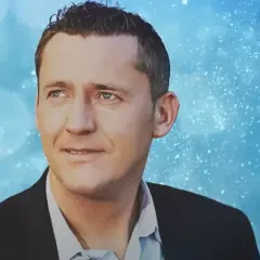 Portret Adama Chroli w garniturze na tle niebieskich, migoczących świateł.