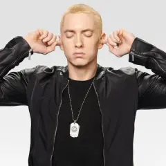 Eminem z zamkniętymi oczami zatyka uszy palcami, ubrany w czarną kurtkę.
