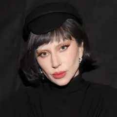 Lady Gaga w czarnym kapeluszu i golfie, z makijażem i biżuterią.