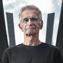 Portret starszego mężczyzny w okularach na tle nowoczesnej architektury.