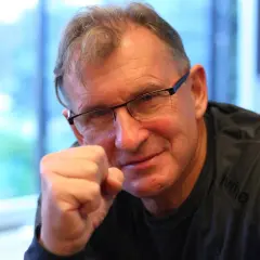 Jerzy Górski w okularach, opierający pięść o policzek, uśmiecha się.