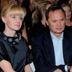 Kobieta w czarnej sukni z ozdobnym kołnierzem i mężczyzna w garniturze siedzą obok siebie.