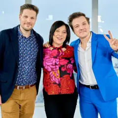 Hanna Śleszyńska z synami, w centrum kobieta w kolorowej bluzce, po bokach dwaj mężczyźni w garniturach.