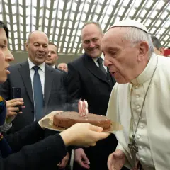 Papież Franciszek zdmuchuje świeczki na torcie urodzinowym, trzymanym przez kobietę.