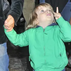 Chłopiec w zielonej kurtce trzyma za rękę dorosłego i wskazuje palcem w górę.