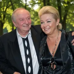 Uśmiechnięta para w eleganckich strojach na tle parku.