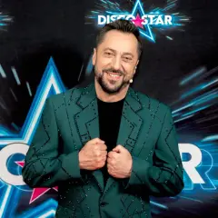 Marcin Miller w zielonej marynarce ozdobionej błyszczącymi kamieniami, uśmiecha się na tle sceny Disco Star.