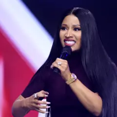 Nicki Minaj z mikrofonem, w ciemnej sukience, z biżuterią na rękach.