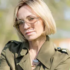 Anna Wyszkoni w okularach i zielonym płaszczu, na tle zieleni.