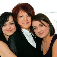 Trzy kobiety: starsza z rudymi włosami w czarnej marynarce i dwie młodsze, córki, obejmujące ją.