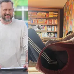 Marcin Prokop w swetrze i z psem na kolanach na tle regału z książkami.