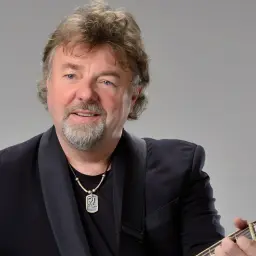 Mariusz Kalaga w czarnym garniturze gra na gitarze.
