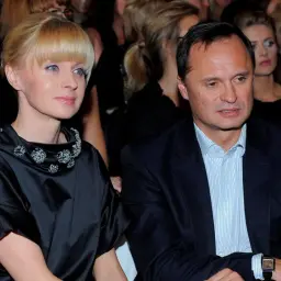 Kobieta w czarnej sukni z ozdobnym kołnierzem i mężczyzna w garniturze siedzą obok siebie.