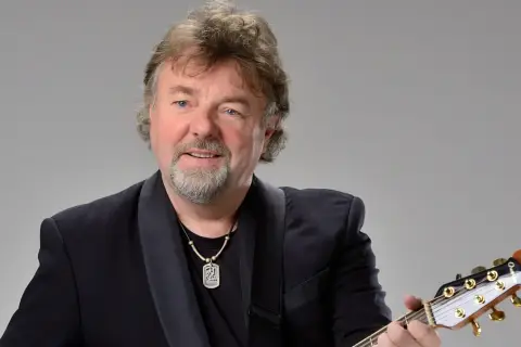 Mariusz Kalaga w czarnym garniturze gra na gitarze.