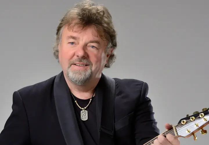 Mariusz Kalaga w czarnym garniturze gra na gitarze.