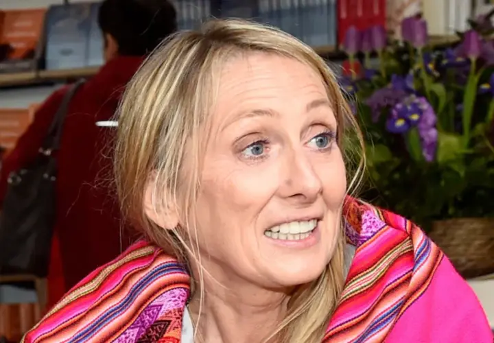 Beata Pawlikowska z kolorowym szalem na tle książek i kwiatów.