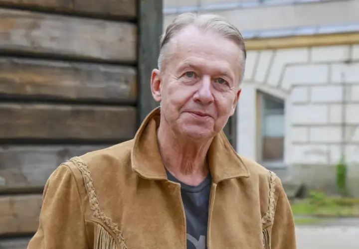 Bogusław Linda w brązowej kurtce z zamszu, z frędzlami i ozdobnymi szwami.