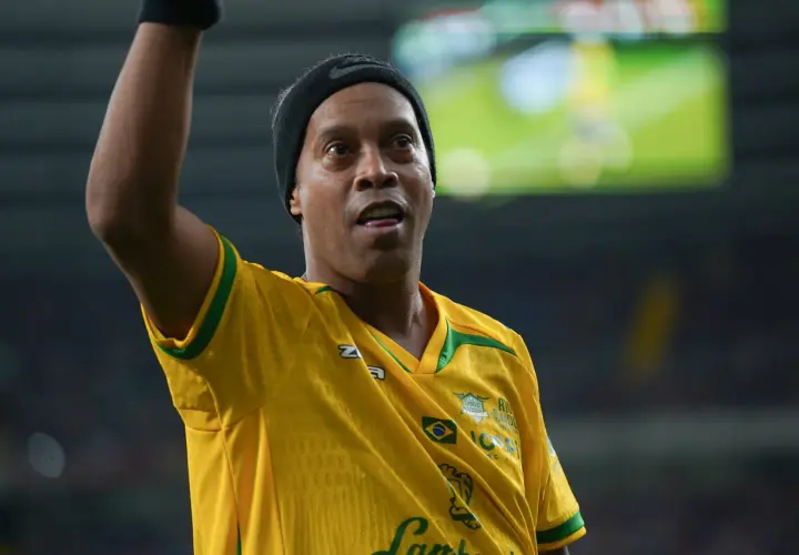 Ronaldinho w żółtej koszulce z zielonymi akcentami, podnosi rękę.