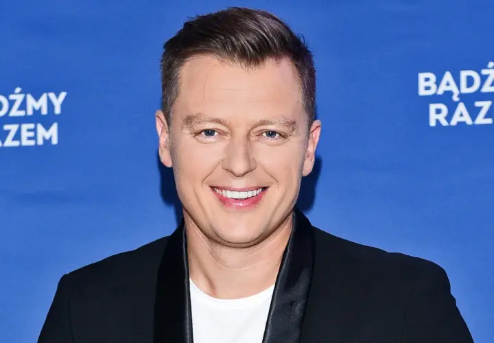 Rafał Brzozowski w czarnym garniturze na niebieskim tle z napisem "Bądźmy razem".