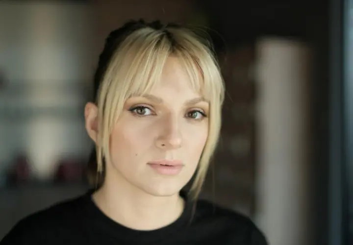 Portret młodej kobiety z blond grzywką i ciemnymi pasemkami włosów, patrzącej w obiektyw.