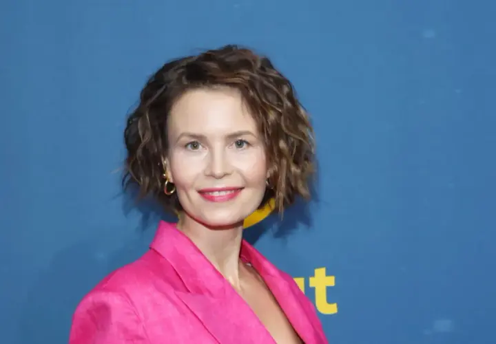 Magdalena Kumorek w różowej marynarce, uśmiechnięta na tle niebieskiego baneru.