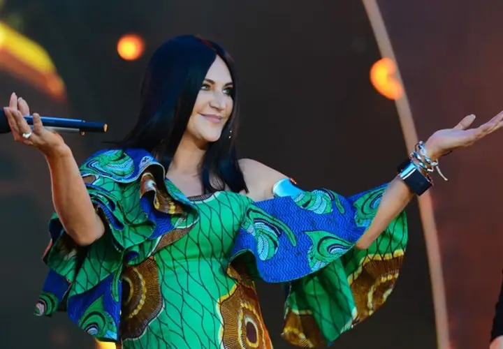 Kayah w kolorowej sukience z falbanami śpiewa na scenie, trzymając mikrofon.