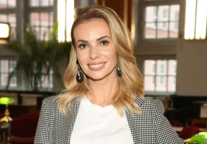 Izabela Janachowska w białej bluzce i marynarce w pepitkę, z czarnymi kolczykami.