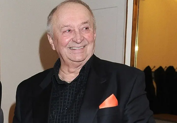 Uśmiechnięty Bohdan Łazuka w czarnym garniturze z pomarańczową poszetką.