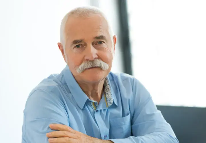 Portret starszego mężczyzny z siwymi włosami i wąsami, w niebieskiej koszuli.