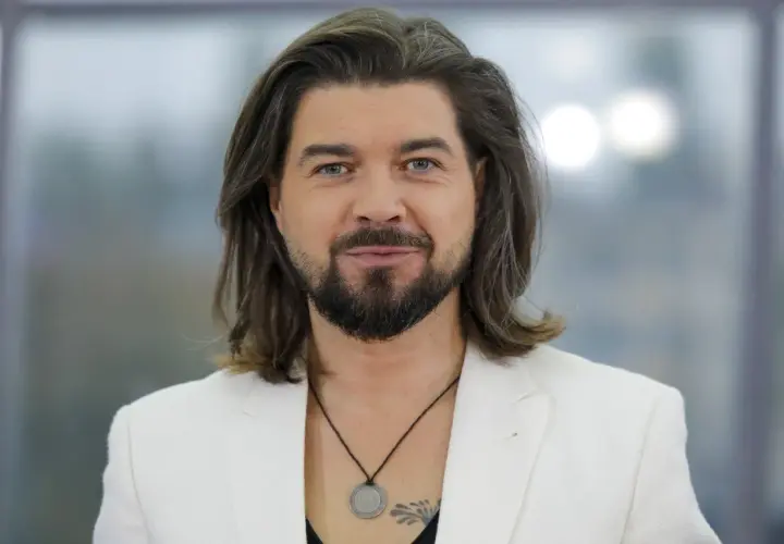 Tomasz Szczepanik w białej marynarce, z długimi włosami i brodą, patrzy w obiektyw.