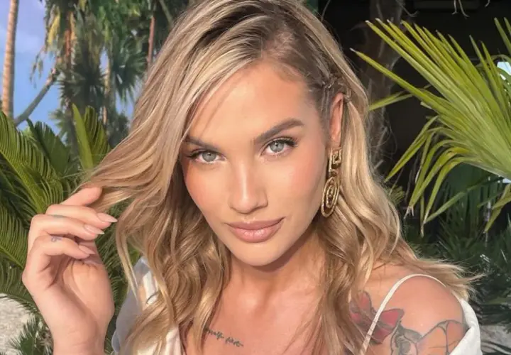 Karolina Gilon z blond włosami, niebieskimi oczami i tatuażem na ramieniu, na tle roślinności.