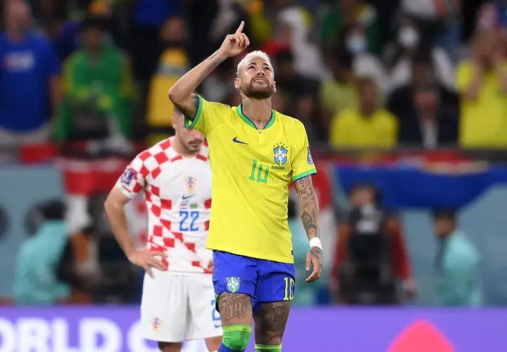 Neymar w żółtej koszulce Brazylii z podniesionym palcem, na tle stadionu.
