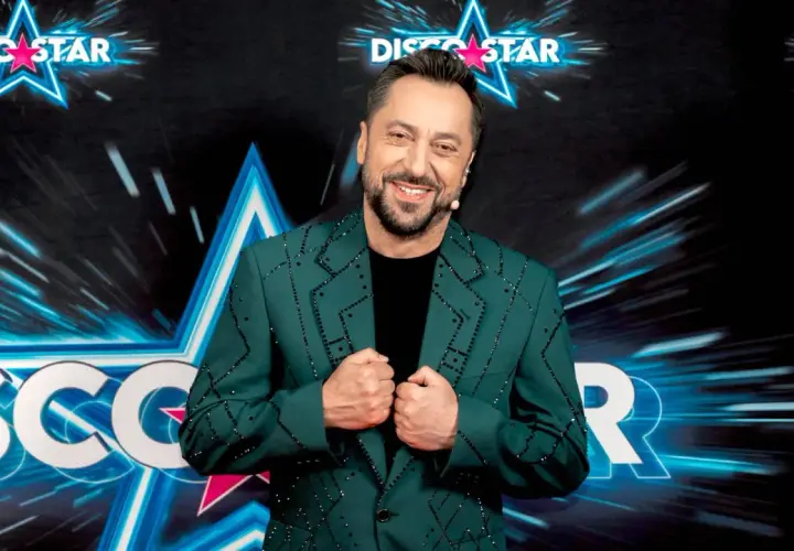 Marcin Miller w zielonej marynarce ozdobionej błyszczącymi kamieniami, uśmiecha się na tle sceny Disco Star.