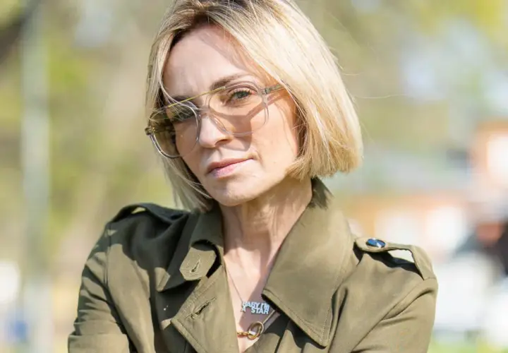 Anna Wyszkoni w okularach i zielonym płaszczu, na tle zieleni.