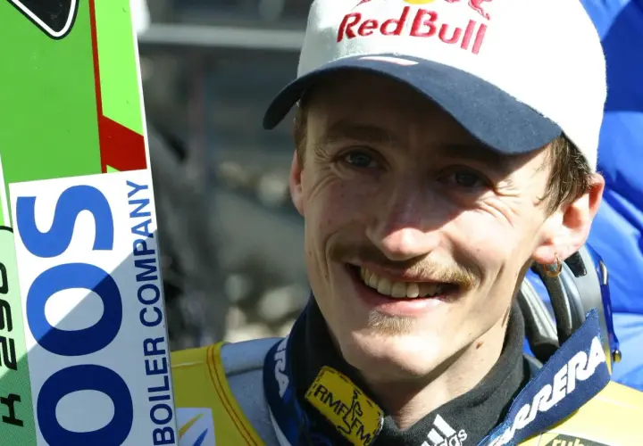 Adam Małysz w czapce Red Bull i z nartami.