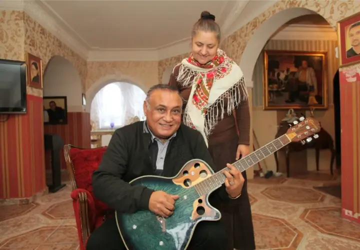 Don Vasyl siedzi z gitarą, obok niego stoi kobieta w chustce.
