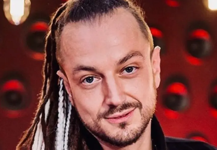 Aleksander Baron z dredami i brodą, na czerwonym tle.