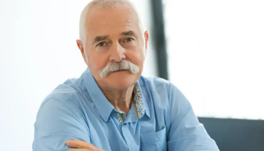 Portret starszego mężczyzny z siwymi włosami i wąsami, w niebieskiej koszuli.