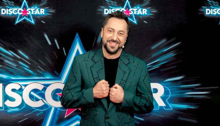 Marcin Miller w zielonej marynarce ozdobionej błyszczącymi kamieniami, uśmiecha się na tle sceny Disco Star.