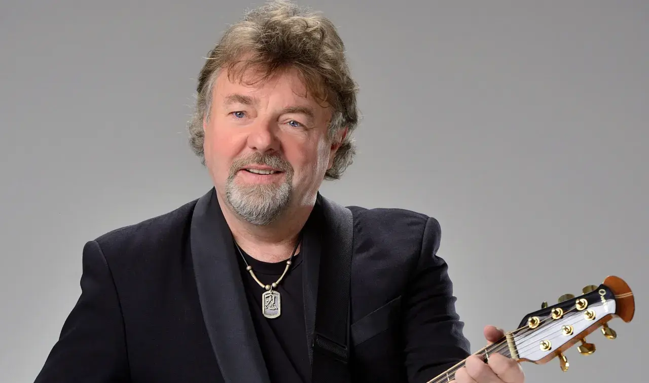 Mariusz Kalaga w czarnym garniturze gra na gitarze.