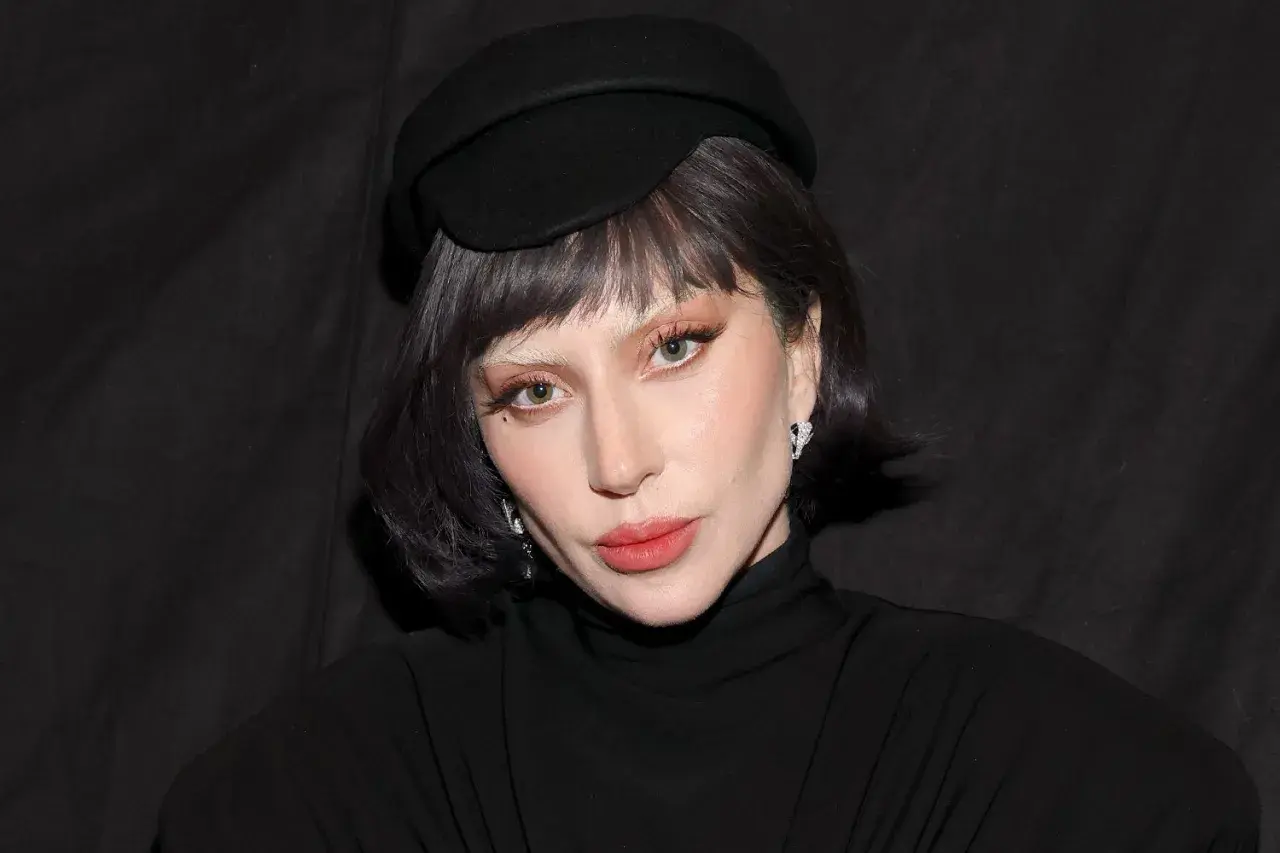 Lady Gaga w czarnym kapeluszu i golfie, z makijażem i biżuterią.