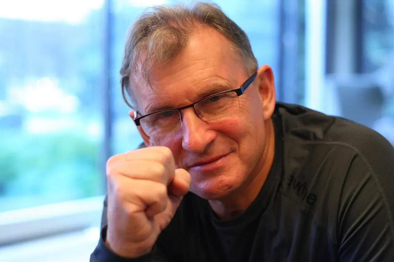 Jerzy Górski w okularach, opierający pięść o policzek, uśmiecha się.