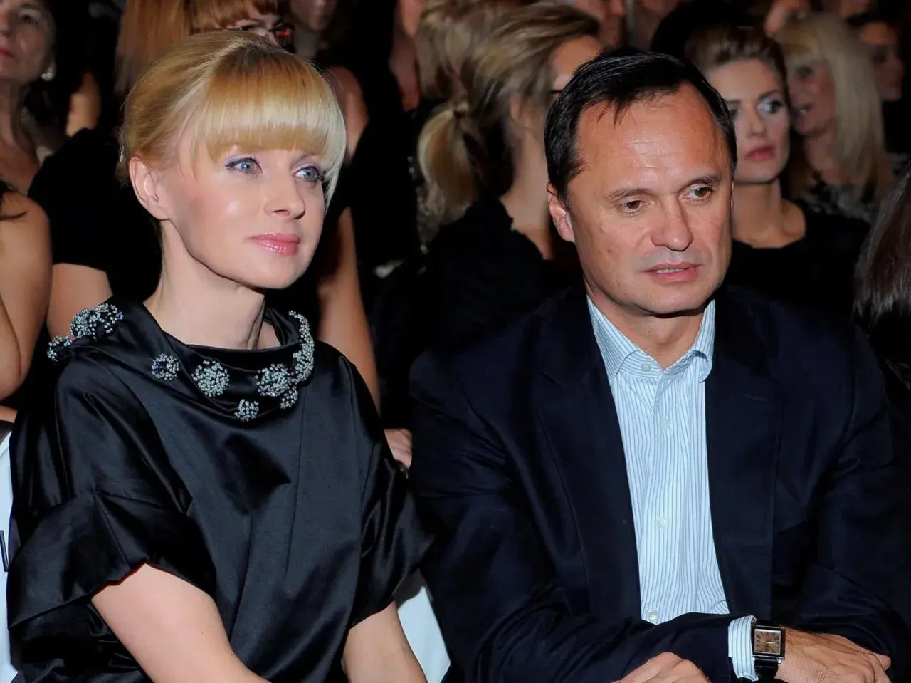 Kobieta w czarnej sukni z ozdobnym kołnierzem i mężczyzna w garniturze siedzą obok siebie.