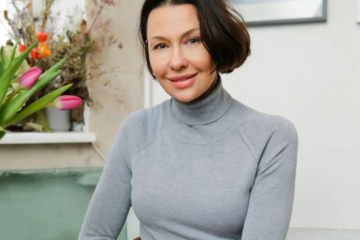 Anna Popek w szarym golfie, z bukietem tulipanów w tle.